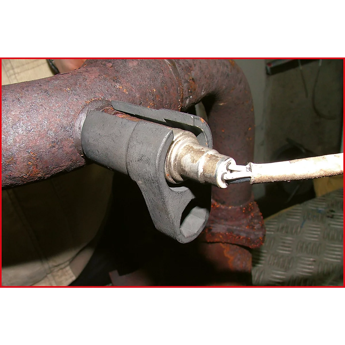 Nahaufnahme einer Lambdasonde, die in einem Auspuffrohr montiert ist. Ein Werkzeug wird zur Installation verwendet.